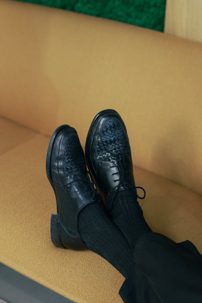 Close-up of black leather shoes on a beige couch, showcasing footwear fashion.